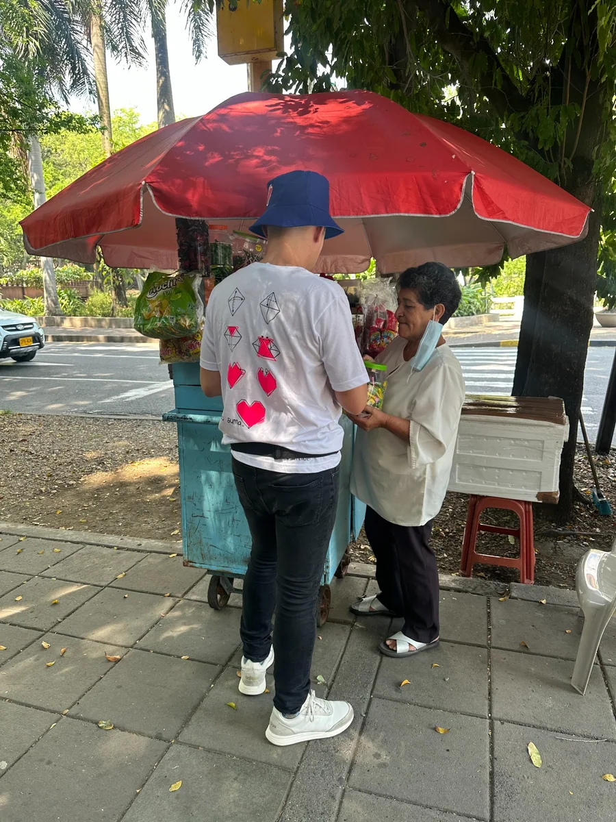 Una persona con camiseta de AMEN conversa con otra junto a un puesto de venta en la calle.